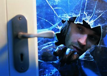 Burglar breaking into a home through a shattered glass door during a burglary attempt